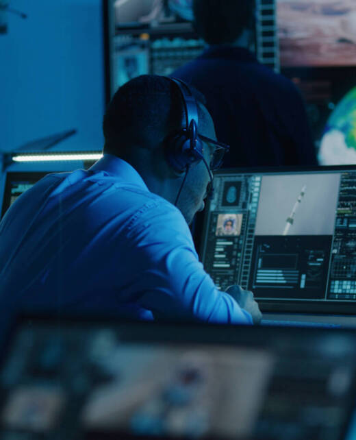 African American flight control employee monitors space mission on multi-monitor computer in mission control center. Team watch successful spacecraft lift off on big digital screen. Space exploration.